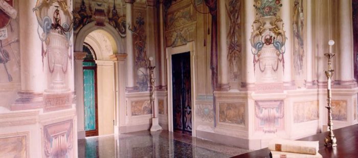 Dettagli di una candela e dei libri sopra una scrivania della Villa di Montruglio, sul fondo una parete affrescata.