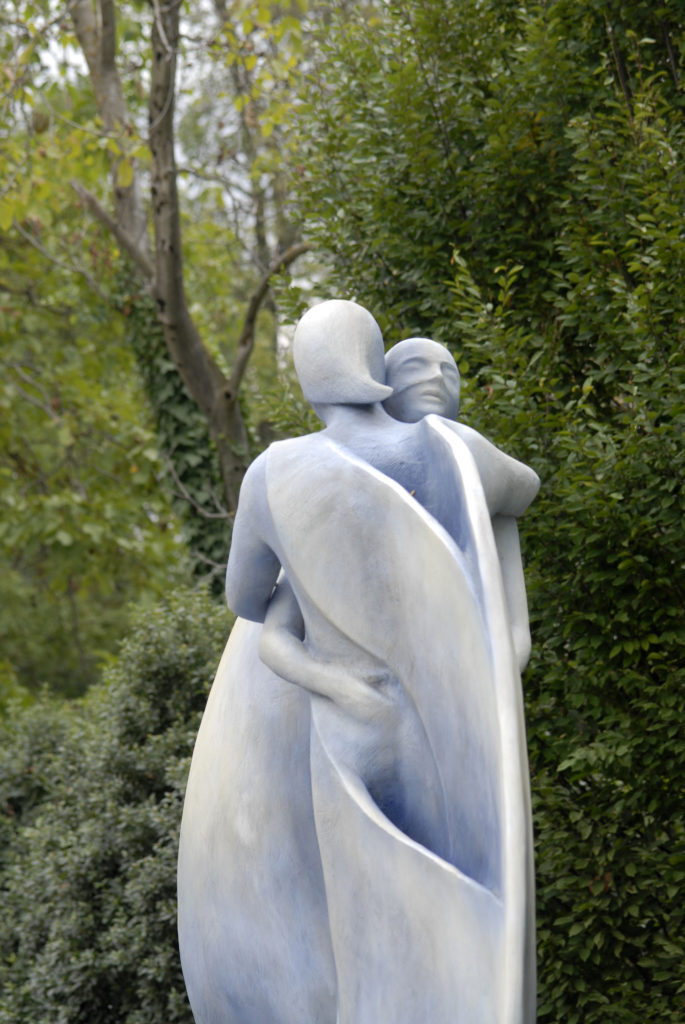 Scultura in pietra di due figure abbracciate nel Parco della Villa di Montruglio. Sullo sfondo dei cespugli.