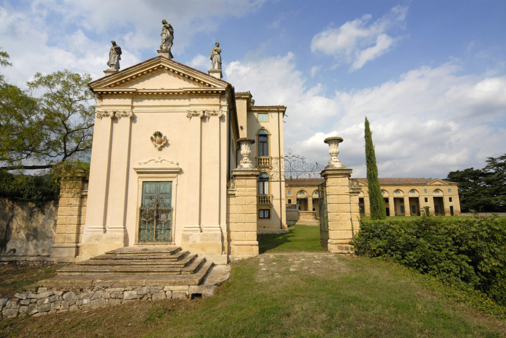 Immagine della Cappella gentilizia laterale della Villa di Montruglio, con dei capitelli colonnali ionici e una piccola scalinata. Di fianco un cancello che porta al Brolo.