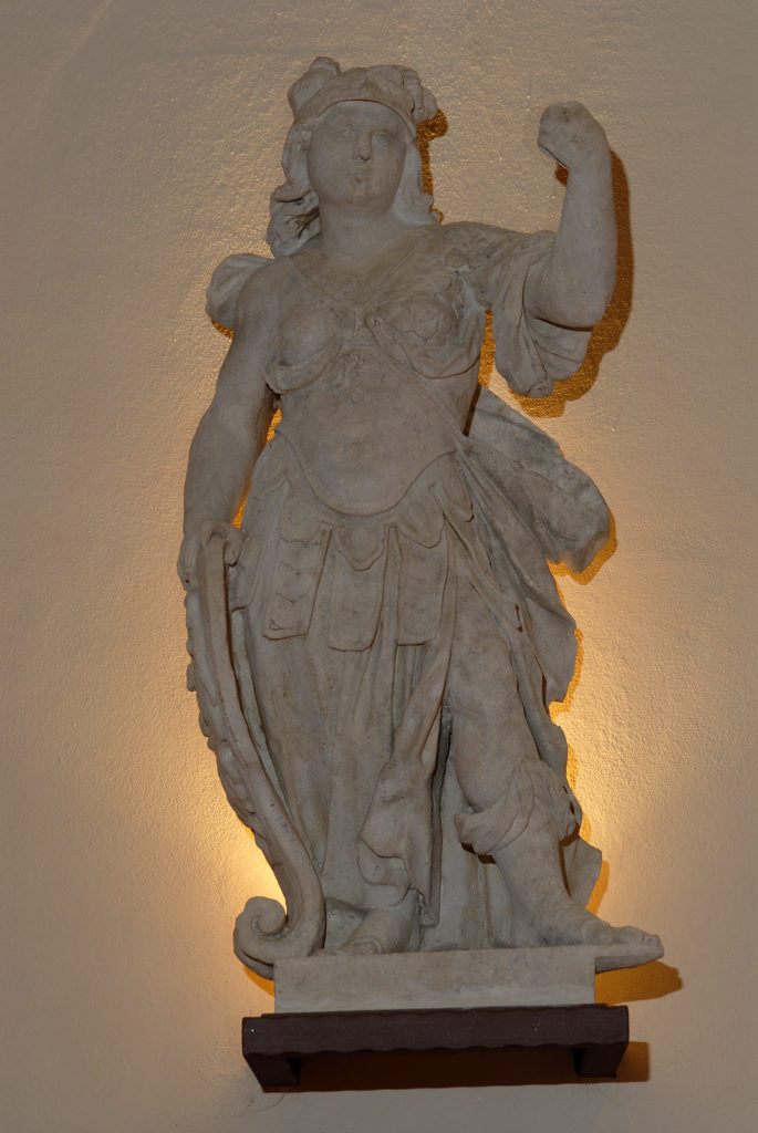 Piccola scultura statuaria posta vicina alla parete su piedistallo aereo, con illuminazione dal basso, nella Villa di Montruglio.
