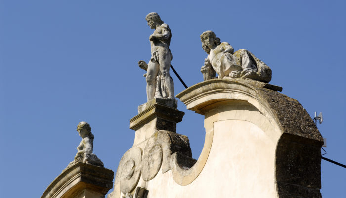 Visione di tre statue sopra il fastigio della Facciata della Villa di Montruglio, che spiccano su di un cielo azzurro.